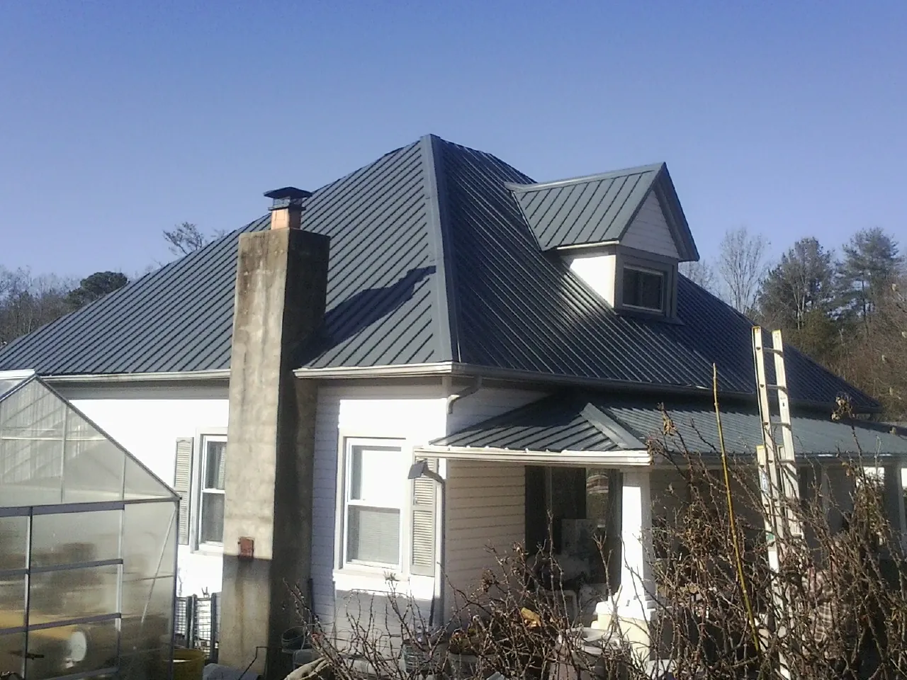 Dark blue standing seam metal roof on a white farmhouse with dormer — Slate & Tile Roof Repair by Roofing Brothers in Lumpkin