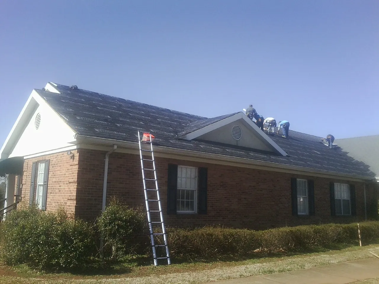Crew tearing shingles off a brick ranch roof with a ladder set — Metal Roof Repair work by our crew in Lumpkin
