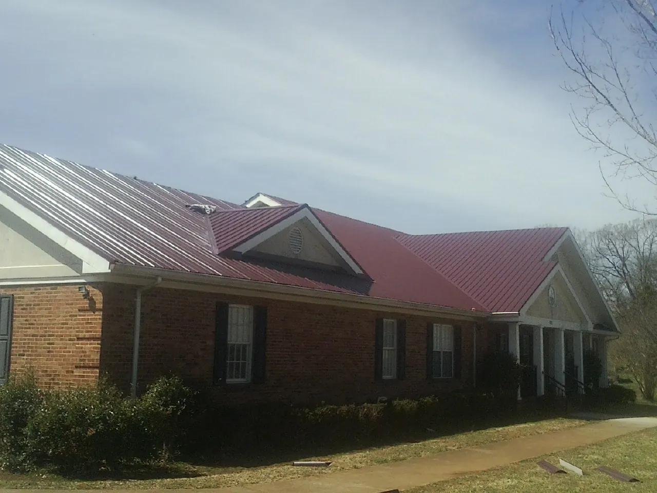 Red metal roof with gabled entries on a long brick building, from a Hail Damage Roof Repair job in Lumpkin