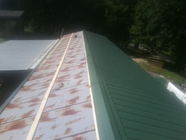 Old rusted panels beside newly installed green metal roofing — Wind Damage Roof Repair by Roofing Brothers in Lumpkin