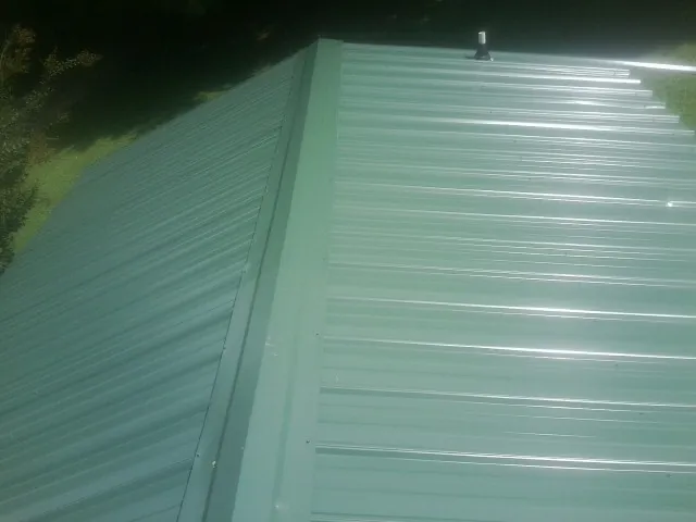 New green metal panels meeting at the ridge of a roof — Flat Roof Repair work by our crew in Lumpkin