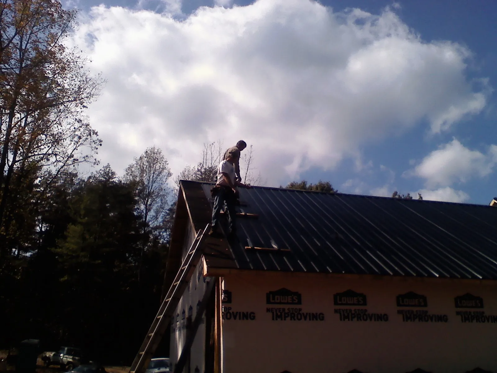 Roofer fastening dark metal panels high against a cloudy sky, from a Roof Inspection job in Lumpkin