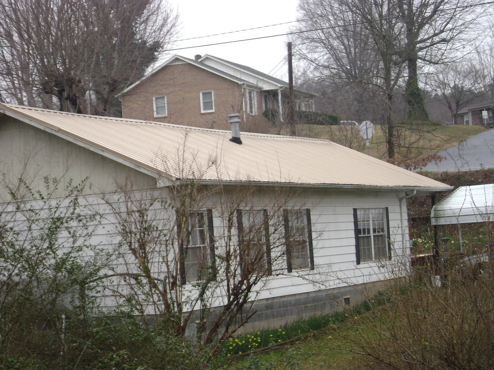 Tan metal roof on a white sided house set into a hillside — Commercial Roofing by Roofing Brothers in Lumpkin